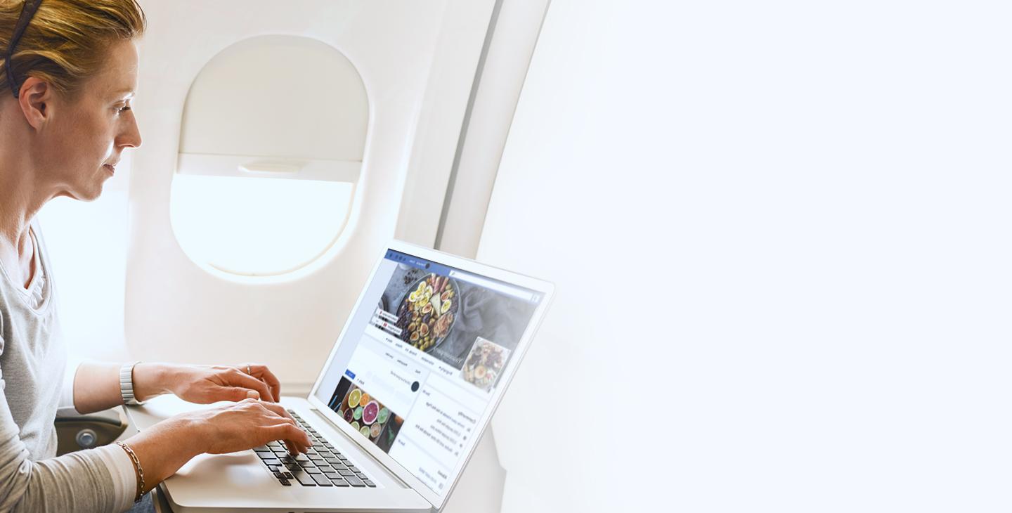 一名女子坐在飞机上，用笔记本电脑上网浏览Facebook